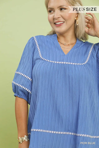 Woman wearing a blue dress with white trim against a green background