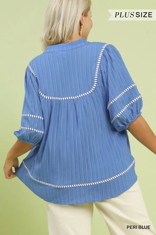 Blue plus-size blouse with white trim on a green background