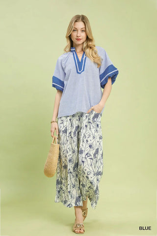 Woman wearing a light blue top with blue trim and floral pants on a light green background