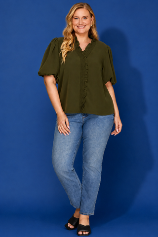 Woman wearing an olive green blouse and blue jeans against a blue background