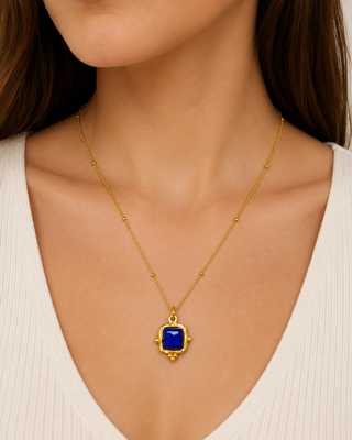 Gold necklace with a blue pendant worn by a person