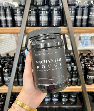 Hand holding a jar of 'Enchanted Rouge' laundry powder with shelves of similar products in the background.
