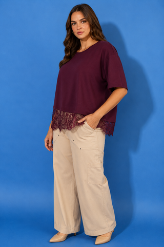 A woman modeling a short-sleeve maroon top with a lace hem, paired with wide-leg beige pants
