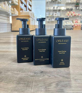 Three bottles of Orleans Luxury Foaming Hand Wash on a wooden surface with a store interior in the background.