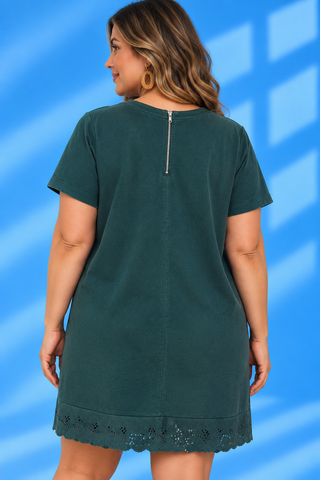 A woman shown from the back wearing a dark teal green short-sleeve tunic dress with a silver zipper at the neckline and a scalloped eyelet hem