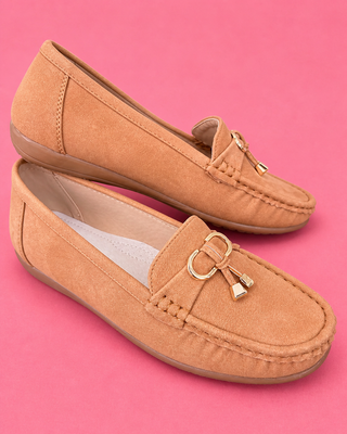 Pair of tan loafers with a decorative buckle on a pink background