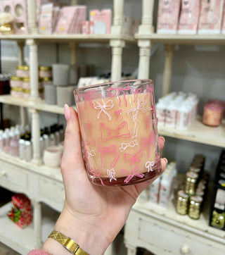 Hand holding a pink candle with decorative designs in a store setting