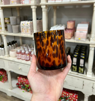 Hand holding a tortoiseshell-patterned candle in front of a store shelf.