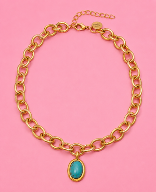 Gold chain necklace with a turquoise pendant on a pink background