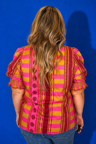 A woman viewed from the back wearing a vibrant pink and yellow striped blouse with red and yellow patterned vertical panels and puff sleeves