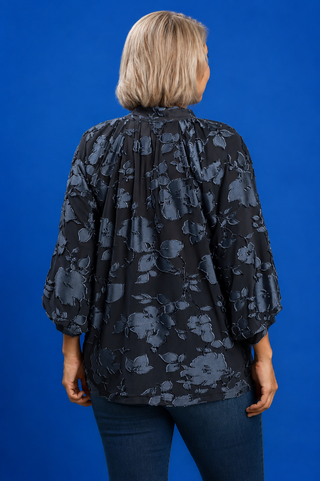 Person wearing a black floral patterned blouse against a blue background