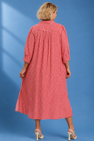 A woman viewed from the back wearing a red and white gingham midi dress with three-quarter sleeves, standing against a solid blue studio background.