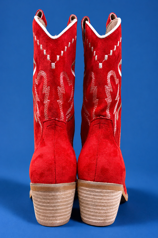 A pair of red suede cowboy boots with white western embroidery and stacked tan wood-look heels, shown from the back against