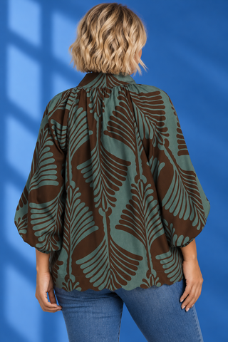 A woman viewed from behind wearing a loose-fitting blouse with a brown and sage green palm leaf pattern