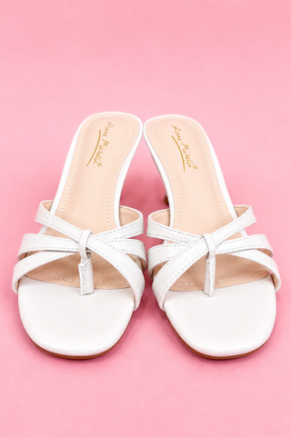 White sandals with thin straps on a pink background