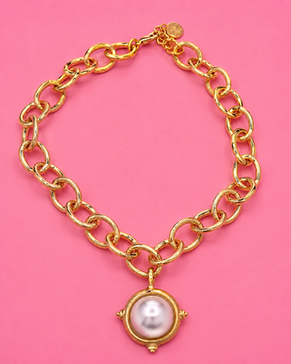 Gold chain bracelet with a pearl charm on a pink background