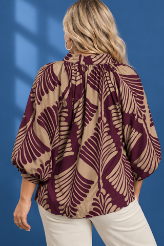 A woman wearing a brown and beige tropical leaf print blouse with balloon sleeves, paired with light blue jeans