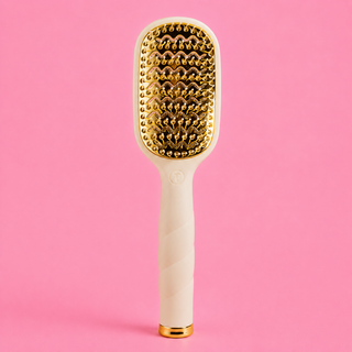 Hairbrush with gold bristle head and handle on a pink background