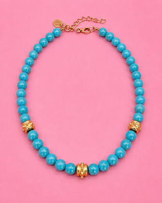 Turquoise beaded necklace with gold accents on a pink background