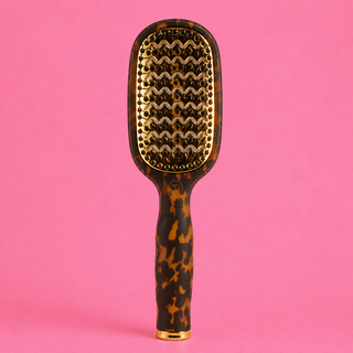 Tortoiseshell paddle brush with gold accents on a pink background