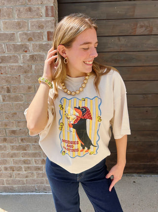 A woman modeling a cream-colored graphic t-shirt with a vintage-style weenie dog print "weenies & martinis