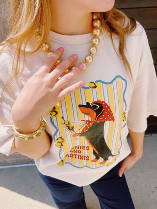 A woman modeling a cream-colored graphic t-shirt with a vintage-style weenie dog print "weenies & martinis