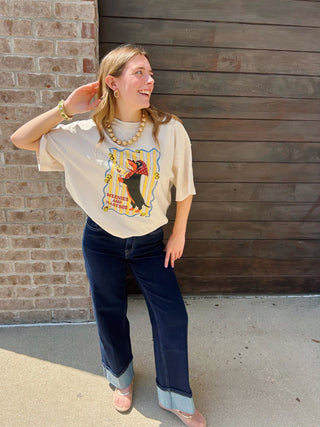 A woman wearing a cream graphic t-shirt with a penguin print, dark blue jeans with cuffed hem