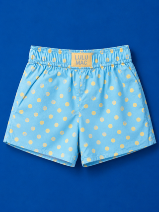 Light blue swim trunks with a yellow polka dot pattern, featuring an elastic waistband with a yellow brand patch that reads 'LULU MAC'.