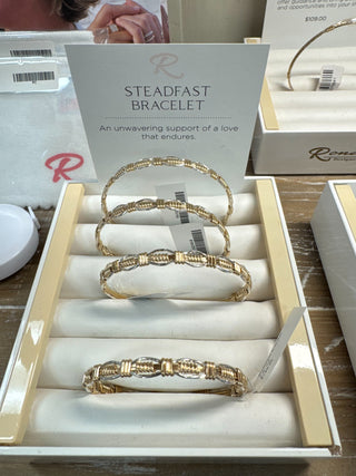Gold bracelets in a box with 'Steadfast Bracelet' packaging.