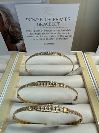 Gold bracelet with silver beads on a display stand with a card describing the 'Power of Prayer' bracelet.