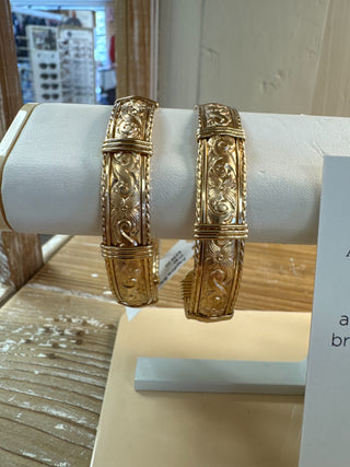 Gold bracelets on a white cylindrical stand with a blurred background