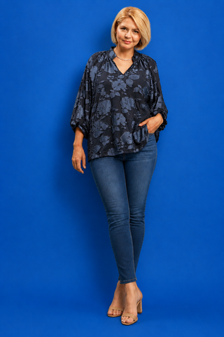 Woman wearing a dark floral blouse and blue jeans against a blue background