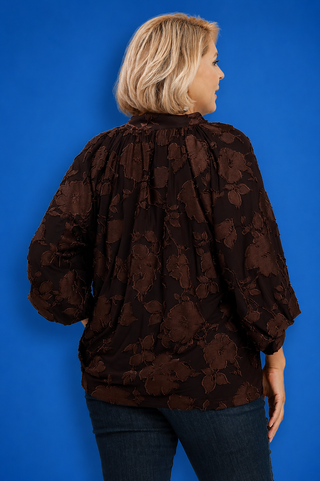 Person wearing a brown floral patterned blouse against a blue background