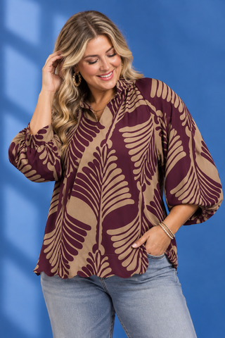 A woman wearing a brown and beige tropical leaf print blouse with balloon sleeves, paired with light blue jeans