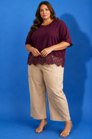 A woman modeling a short-sleeve burgundy top with a lace hem and beige cropped pants