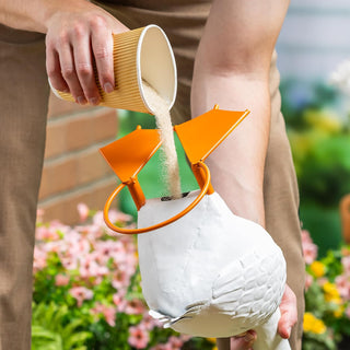 Person pouring a substance into a white container with an orange funnel outdoors.