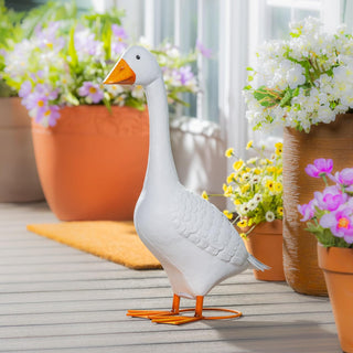 Decorative goose statue on a wooden surface with potted plants in the background