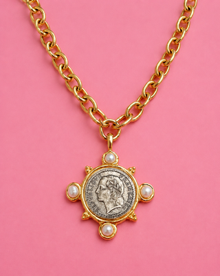 Gold necklace with a coin pendant on a pink background