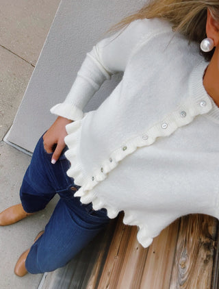 Ivory knit cardigan with ruffle trim, pearl-style buttons, ruffled hem, and feminine flared cuffs