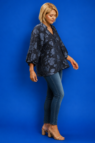 Woman wearing a dark floral blouse and blue jeans against a blue background