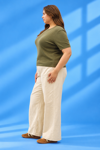 A woman stands in profile wearing an olive green short-sleeve t-shirt and cream wide-leg pant