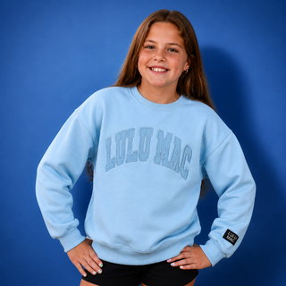 Person wearing a light blue 'LULU MAC' sweatshirt against a blue background