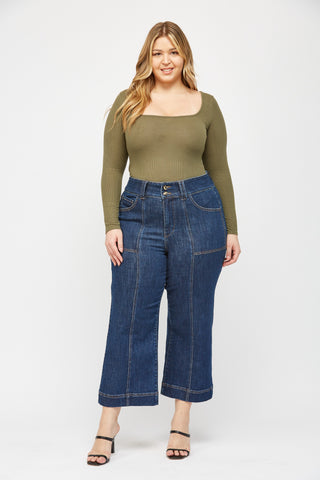Woman wearing an olive green top and blue jeans on a white background