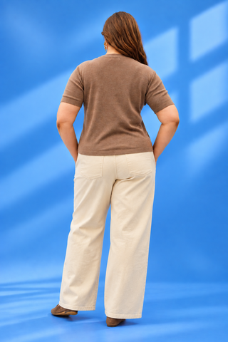 A woman is shown from behind wearing a brown short-sleeve knit top and cream wide-leg trouser