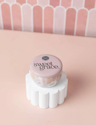 Container labeled 'sweet grace' on a white stand with a pink and white striped background
