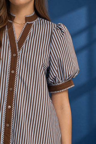 A woman modeling a short-sleeve button-up shirt with vertical blue and white stripes, brown trim