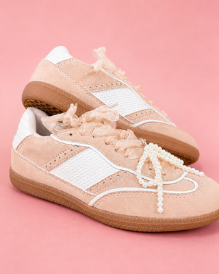 Beige sneakers with pearl-like laces on a pink background