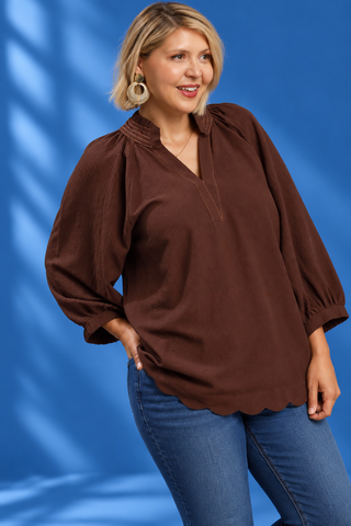 A woman modeling a brown long-sleeve blouse with a split V-neckline and gathered sleeves, paired with blue jeans 