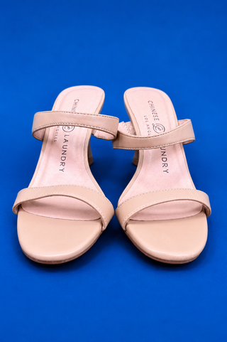 A pair of light pink leather slingback mule sandals with a kitten heel, displayed on a solid blue
