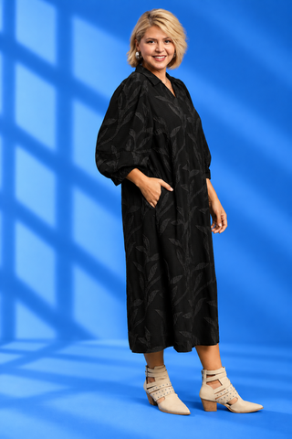 A woman modeling a black midi-length collared dress with a subtle tonal leaf pattern